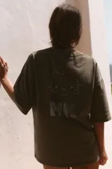 Remera oversize de color marrón grisáceo con efecto lavado, cuello redondo y manga corta. Cuenta con múltiples aplicaciones de brillos con motivos de Hello Kitty, estrellas, cerezas y moños.