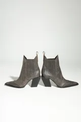 Bota tejana de cuero color gris oscuro con efecto desgastado, punta fina y taco cuadrado. Presenta paneles laterales elásticos con costuras decorativas verticales.