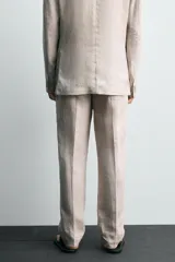 Pantalón de traje regular fit confeccionado en tejido de lino, con bolsillos laterales y bolsillos traseros de vivo con botón. Presenta cierre frontal con cremallera y botón.