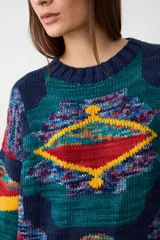 Sweater de tejido de punto con diseño geométrico multicolor sobre base azul marino, cuello redondo y puños acanalados.