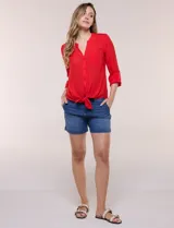 Blusa de calce relajado color salmón, confeccionada en tela liviana con textura sutil. Presenta escote en V con abotonadura frontal, bolsillo parche en el pecho, mangas largas regulables con presilla y ruedo con opción de anudar en el frente.