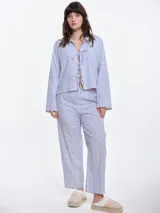 Camisa de dormir de popelina de algodón, con estampado de rayas verticales y pequeños motivos geométricos. Presenta cuello camisero, mangas largas y cierre frontal mediante lazos ajustables.