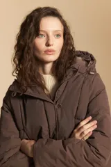 Campera acolchada de nylon en color crema, con capucha ajustable, cierre frontal con botones y cordón de ajuste en la cintura.