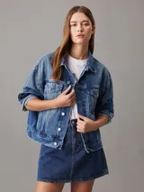 Campera de denim azul medio vintage, corte relaxed boxy, confeccionada con 20% de algodón reciclado. Tiene cuello en punta, bolsillos de parche en el pecho, bolsillos de hendidura en la cintura, botones metálicos de la marca y parche con logo de Calvin Klein en el bolsillo del pecho.