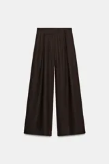 Pantalón de tiro alto y pernera ancha, color marrón, con pinzas delanteras, bolsillos frontales y cierre con cremallera y botón.