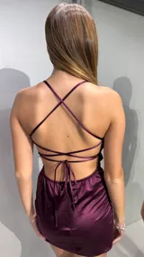 Vestido corto bordó satinado, con escote recto y tirantes finos cruzados en la espalda.