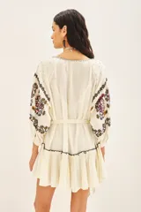 Vestido corto de bambula color celeste, con escote redondo, mangas tres cuartos abullonadas y falda con volado en el ruedo. Presenta bordados decorativos en el frente y las mangas, y cuenta con un cinturón de la misma tela para ajustar a la cintura.