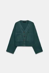 Chaqueta de punto color verde oscuro, con escote en pico, manga larga y cierre frontal con botones. Presenta dos bolsillos de plastrón en la parte delantera.