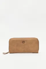 Billetera de formato rectangular con cierre perimetral, confeccionada en material símil cuero de textura suave. Presenta un aplique metálico circular con logo grabado en el frente y tirador de cierre en el mismo material.