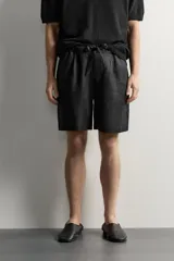 Bermuda de lino negro de corte relaxed fit, con cintura elástica ajustable mediante cordón y bolsillos frontales.