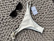 Bombacha de bikini colaless, color crudo texturizado en la parte trasera y negro brillante en la parte delantera. Tiene tiras regulables en los laterales.
