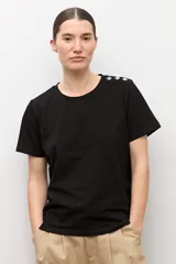 Remera blanca de manga corta con detalle de botones metálicos en el hombro, cuello redondo y corte clásico.