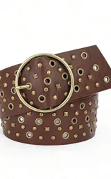 Cinturón marrón de cuero sintético con tachas y ojalillos metálicos dorados y hebilla circular dorada.