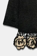 Top de punto negro con cuello redondo y manga corta. Presenta un diseño de tejido calado en el bajo con aplicaciones estructurales en forma de flores en color beige.