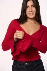Blusa de algodón color beige con escote en V y detalle de argolla metálica en el centro del pecho. Presenta mangas largas con terminación oxford acampanada y diseño ajustado al cuerpo.
