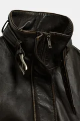 Cazadora de cuero con efecto desgastado, cuello subido con trabilla y hebilla metálica, manga larga y cinturón ajustable en la cintura con hebilla metálica. Presenta cierre frontal con cremallera oculta y bolsillos laterales.