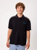 Remera polo Rusty de corte holgado, color negro con detalles en gris en los hombros y mangas, línea blanca divisoria y logo bordado en celeste en el pecho. Cuenta con cuello clásico y cierre frontal de botones.