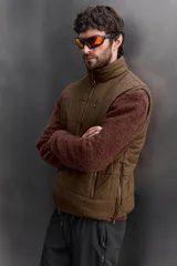 Chaleco marrón acolchado con cuello alto, cierre frontal con cremallera, bolsillos laterales con cremallera y bajo ajustable con trabilla y cremallera lateral.