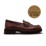 Zapato tipo mocasín de cuero color marrón con textura granulada, suela track de goma y detalle de herraje metálico dorado en el empeine.