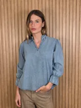 Blusa de jean color celeste, con escote en V y cuello mao con volados sutiles. Presenta mangas largas abullonadas con puños elastizados y diseño holgado.