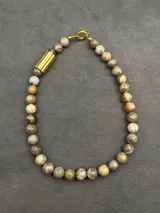 Collar de piedras naturales en tonos tierra, con detalle de tubo dorado en un lateral y cierre marinero dorado.