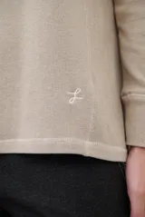 Remera de manga larga en color beige, confeccionada en tejido de punto con costuras a la vista en contraste. Presenta un corte holgado, cuello redondo y un pequeño bordado distintivo en la parte inferior.