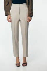 Pantalón de tiro alto color beige, con detalle de costuras marcadas en el delantero y la espalda. Incluye bolsillos delanteros de vivo y cierre frontal con cremallera, botón interior y gancho metálico.