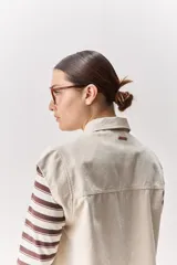 Chaleco de algodón color beige, de calce relajado, con cuello clásico, hombros amplios, cierre frontal con broches metálicos y bolsillos delanteros con solapa.