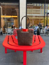 Bolso tipo tote bag de cuero trenzado a mano, en tonos marrón y negro, con asas trenzadas.