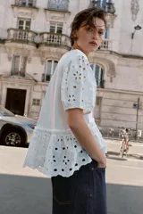 Camiseta blanca de manga corta abullonada y cuello redondo, con detalles de bordados perforados y bajo con doble volante.