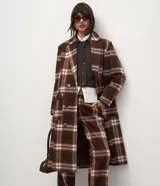 Trench coat largo de corte clásico con estampado de cuadros en tonos marrones y beige. Presenta cuello con solapas, cierre frontal con botones, mangas largas y bolsillos laterales aplicados.