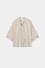 Camisa de corte holgado confeccionada en mezcla de lyocell, con estampado de rayas verticales en tonos neutros y azules. Presenta cuello redondo con lazada frontal, cierre con botones ocultos y mangas amplias por debajo del codo.