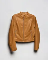 Campera estilo motero de símil cuero color habano, con cuello mao, cierre frontal, calce entallado y detalles de tachas en hombros y mangas.