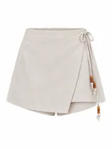 Short pollera de tiro alto símil lino color beige, con diseño cruzado tipo falda envolvente y lazos laterales decorados con cuentas de madera.