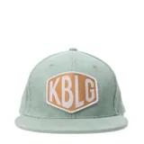 Gorro tipo cap de pana color verde agua, con parche frontal hexagonal en color tostado con letras blancas.