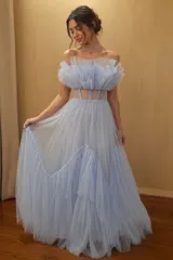 Vestido largo de tul color celeste, con diseño strapless y escote con volados plisados. Presenta una cintura con paneles transparentes tipo corset y una falda amplia con volados en capas.