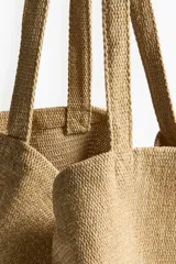 Bolso de playa tipo tote de tejido texturizado en color beige, con dos asas superiores para llevar al hombro.