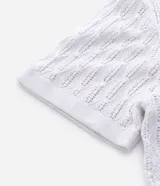 Polo de manga corta color blanco, con cuello en V y textura de rombos abiertos. Confeccionado en algodón.