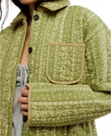 Chaqueta acolchada de algodón, color verde lima con estampado floral en rayas verticales en tono más claro. Presenta cuello clásico, cierre frontal de botones oscuros y un bolsillo de parche en el pecho con ribete en color beige.