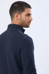 Buzo de punto texturado color azul marino, con cuello alto y cierre frontal parcial. Presenta puños y ruedo acanalados, con un pequeño logo bordado en el pecho.