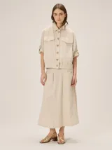 Falda midi de lino color beige con sutiles líneas a cuadros, tiro alto, diseño amplio con pliegues frontales y bolsillos laterales.