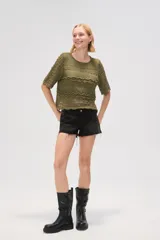 Remera de tejido de punto calado en color natural, con cuello redondo y mangas cortas. Presenta un diseño con texturas de ondas horizontales y terminaciones festoneadas.