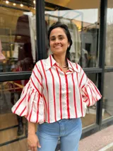 Camisa de seda sintética con estampado de rayas verticales blancas y rojas, cuello camisero, cierre frontal de botones y mangas cortas abullonadas con volumen.