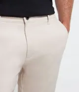 Pantalón de vestir para hombre, color beige claro, de corte slim y sastrería. Presenta cierre frontal con botón y cremallera, y bolsillos laterales y traseros.