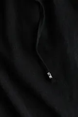 Pantalon negro de tiro bajo confeccionado en mezcla de lino y viscosa, con cintura elastizada, cordon de ajuste frontal con cuentas decorativas, piernas rectas y bolsillos laterales.