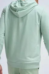 Chaqueta deportiva con cierre frontal completo, capucha con cordones ajustables y bolsillos tipo canguro, confeccionada en tejido de algodón en color verde menta.