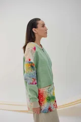 Campera larga con cierre metálico y bolsillos grandes, de color verde con mangas y parte inferior estampadas con diseño abstracto multicolor.