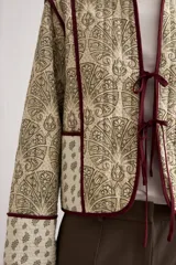 Chaqueta capitoneada de diseño acolchado con estampado paisley en tonos beige y verde, con ribetes y lazos de cierre frontales en color bordó.