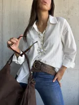 Camisa blanca de corte clásico con textura de rayas verticales sutiles, cuello camisero, cierre frontal de botones y mangas largas con puños.