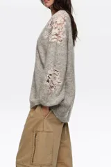 Cardigan gris melange de punto con escote en V y cierre frontal de botones. Presenta aplicaciones de encaje en tono rosado en el hombro izquierdo y en el lateral inferior derecho.